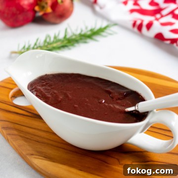 Pomegranate-Port Gravy with Rosemary for Roasts and Poultry 16 Pomegranate gravy in a white gravy boat with a white handled spoon with pomegranates in the background.