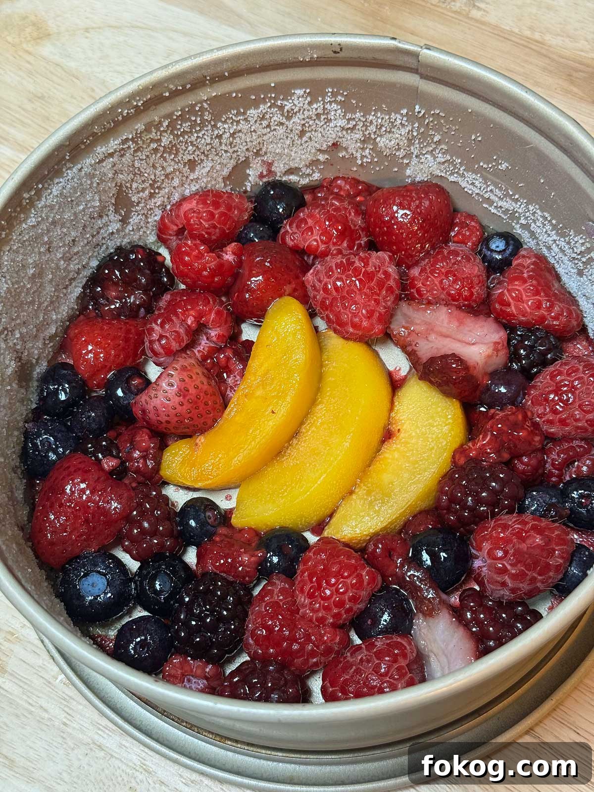 A springform pan greased with olive oil and dusted with granulated sugar with fruit on the bottom for an Upside Down Olive Oil Cake.