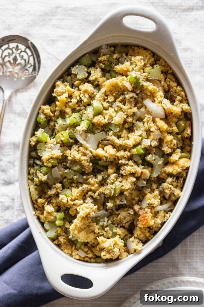 a cream, oval casserole dish of gluten free cornbread stuffing next to a silver serving spoon
