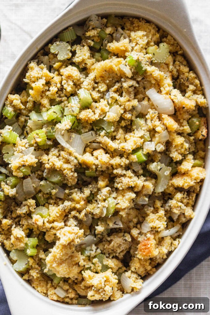 a cream, oval casserole dish of gluten free cornbread stuffing next to a silver serving spoon