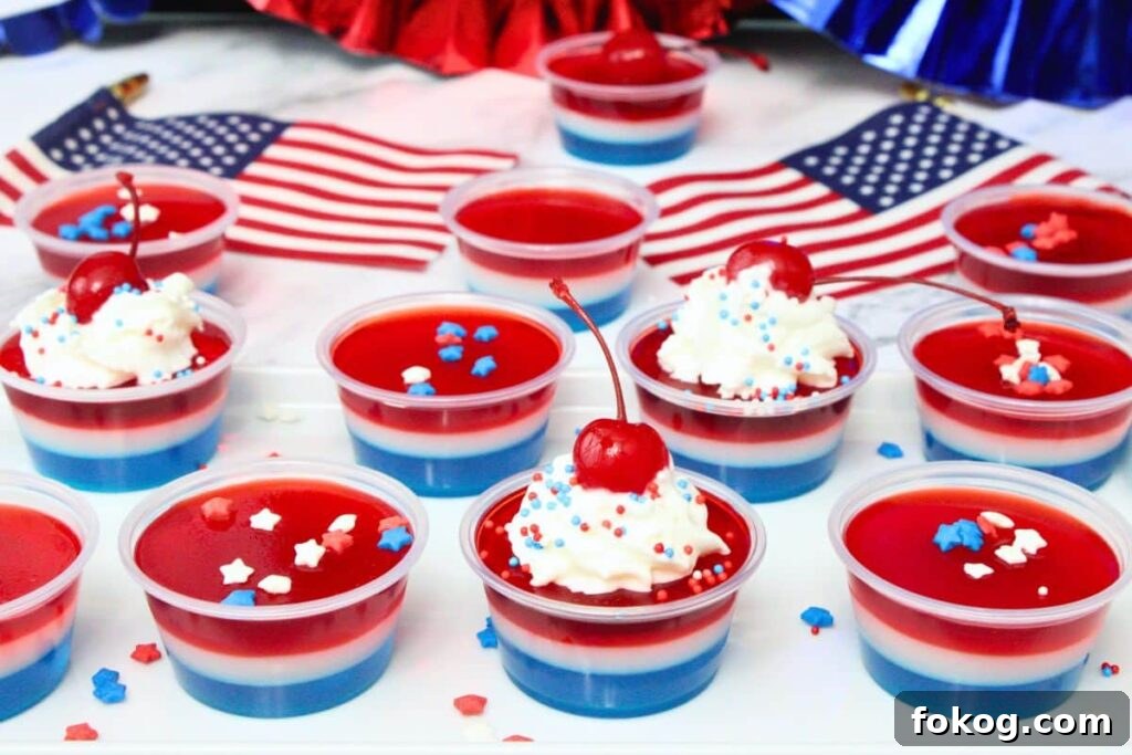 several red white and blue jello shots topped with whipped cream and a cherry surrounded by patriotic decor