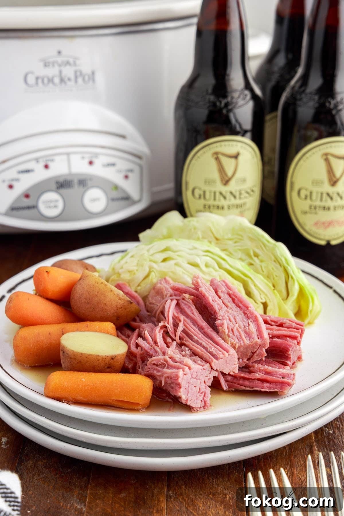 Platter of Slow Cooker Corned beef and cabbage with bottles of Guinness in the background.