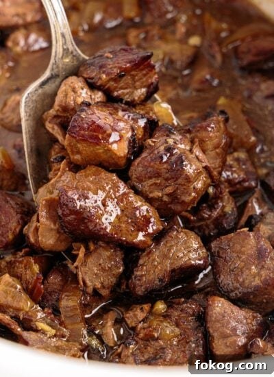 Spoon lifting cooked crockpot steak bites from crock.