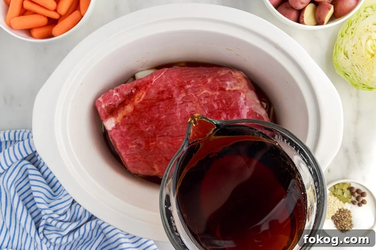 Mixed sauce in a bowl being poured into the crock pot over the brisket, other ingredients in the background.