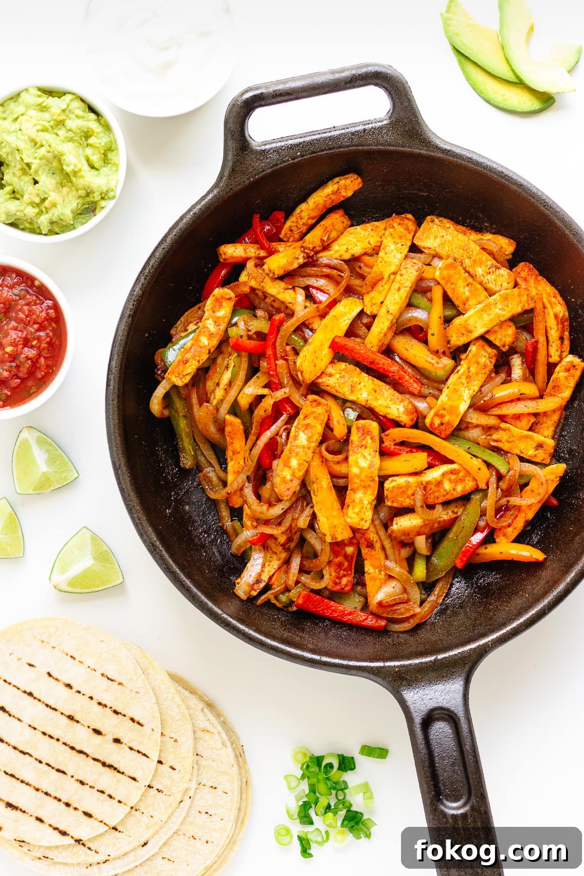 Grilled Halloumi Fajitas with Peppers and Lime crema 2 Flat lay of halloumi vegetable fajita mixture in a cast iron skillet surrounded by tortillas and toppings.
