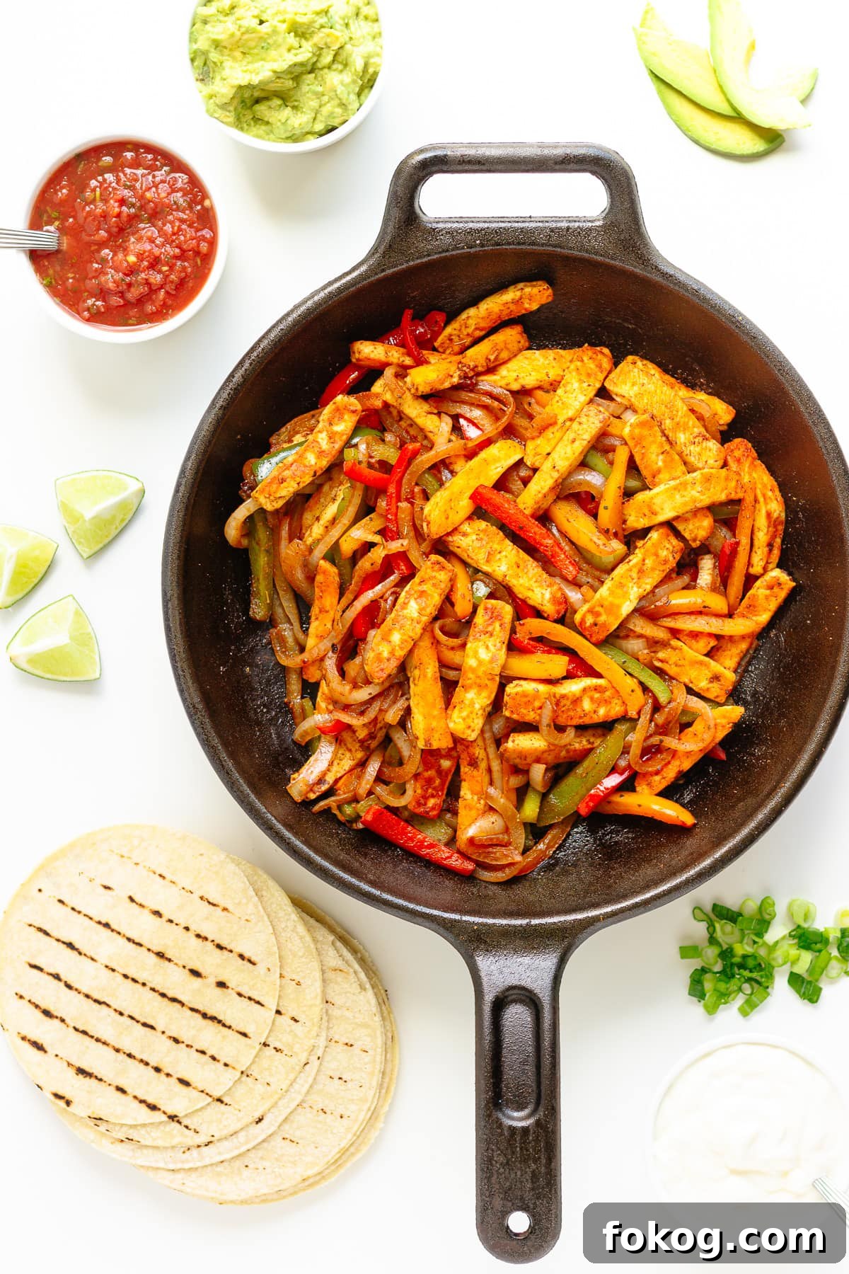Grilled Halloumi Fajitas with Peppers and Lime crema 12 Halloumi veggie fajita mixture in a cast iron skillet with tortillas and a variety of toppings around it.