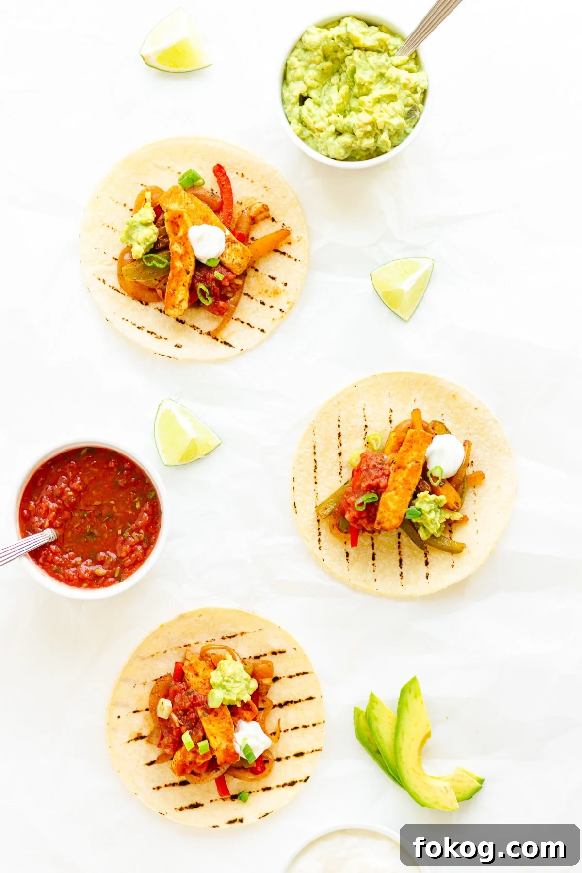 Grilled Halloumi Fajitas with Peppers and Lime crema 3 Three halloumi fajitas on a white background with various toppings laid out around them.