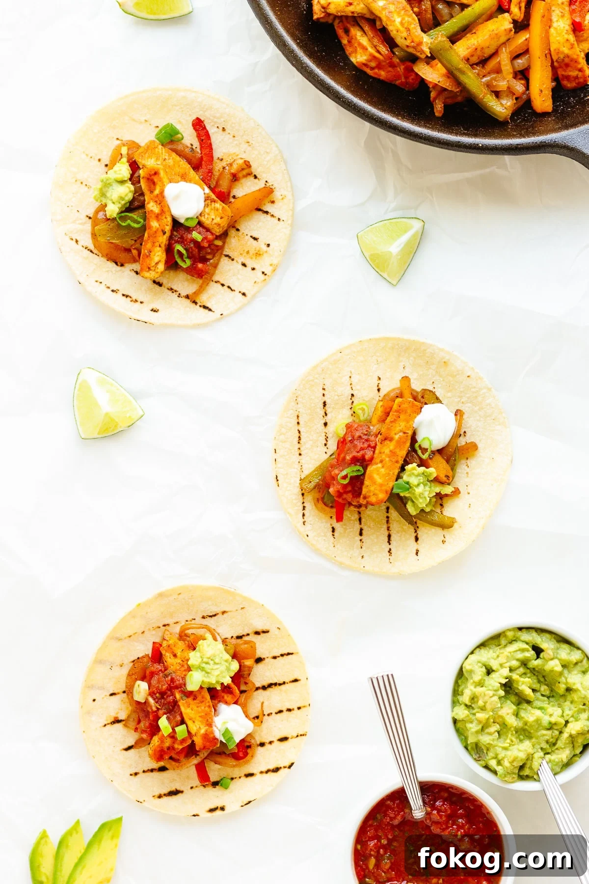 Grilled Halloumi Fajitas with Peppers and Lime crema 10 Three topped halloumi vegetable fajitas with a skillet of the mixture and toppings around them.