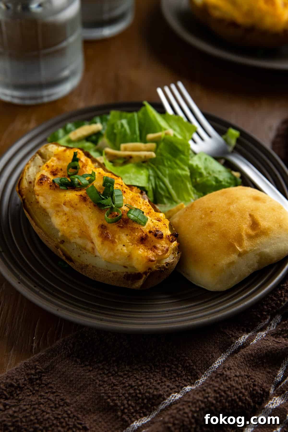 Shrimp-Stuffed Baked Potatoes with Garlic Butter Filling 2 Two baked potato halves on brown plate with roll and side salad.