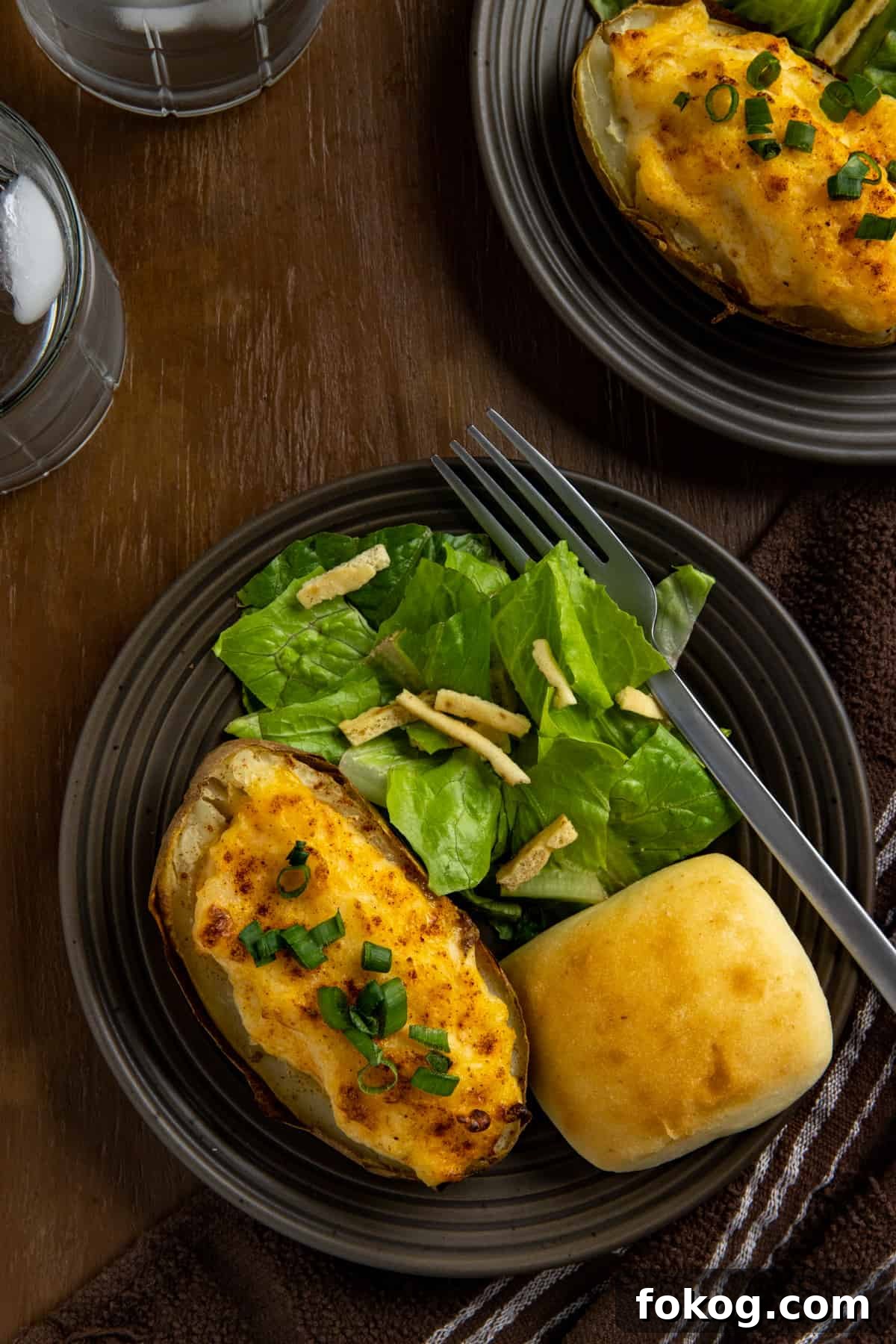 Shrimp-Stuffed Baked Potatoes with Garlic Butter Filling 5 Two baked potato halves on brown plate with roll and side salad.