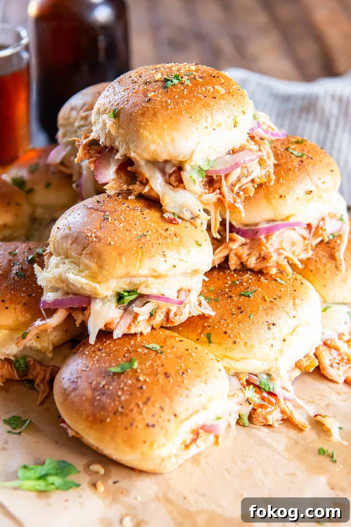 A stack of BBQ chicken sliders on parchment paper.
