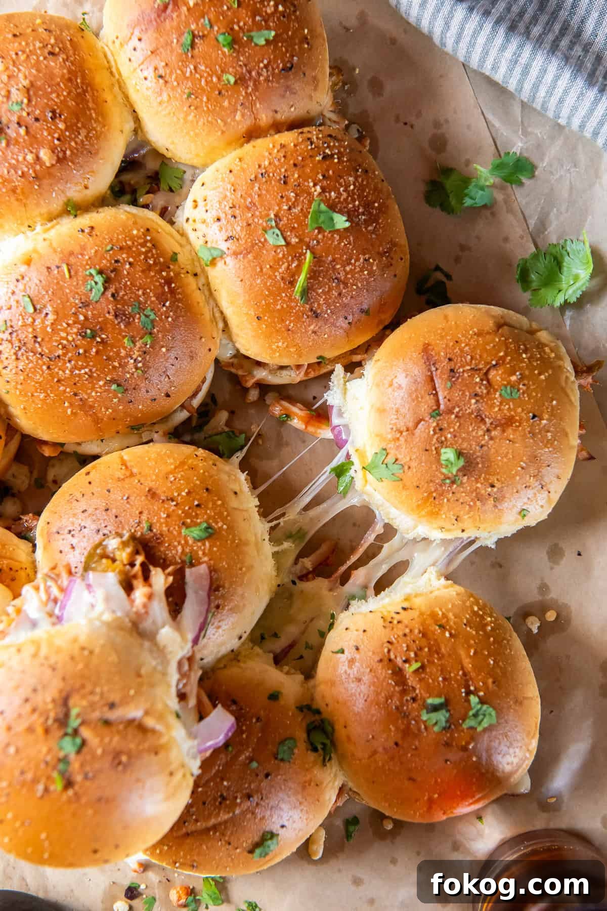 BBQ chicken sliders with melted cheese on parchment paper.