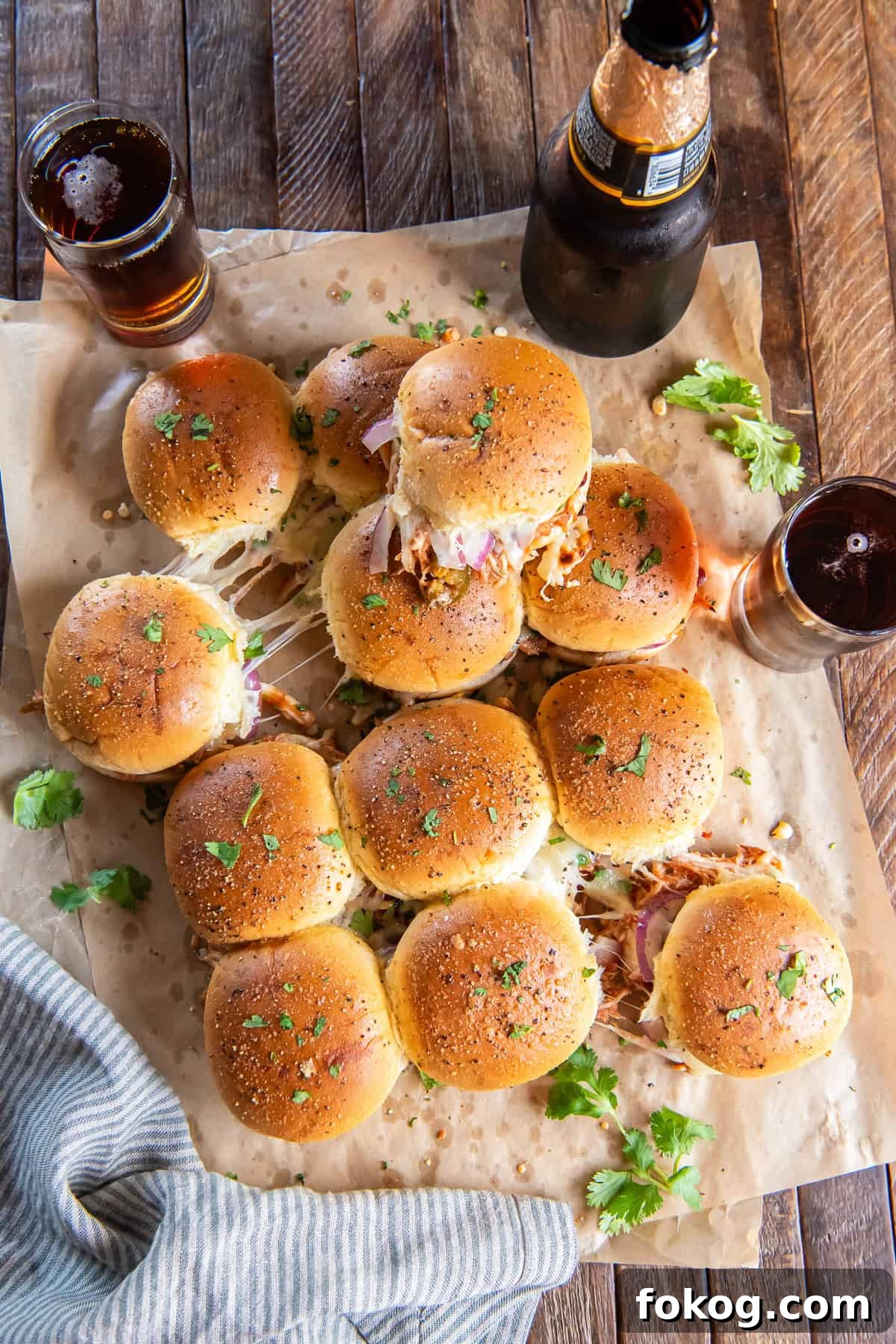 BBQ chicken sliders on parchment paper with bottle of beer nearby.