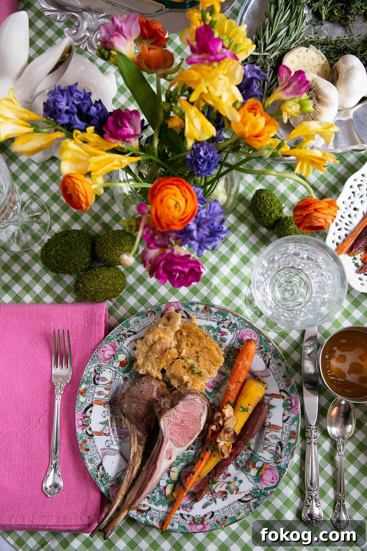 gingham tablecloth topped with a china plate of easter dinner and a vase of colorful flowers.