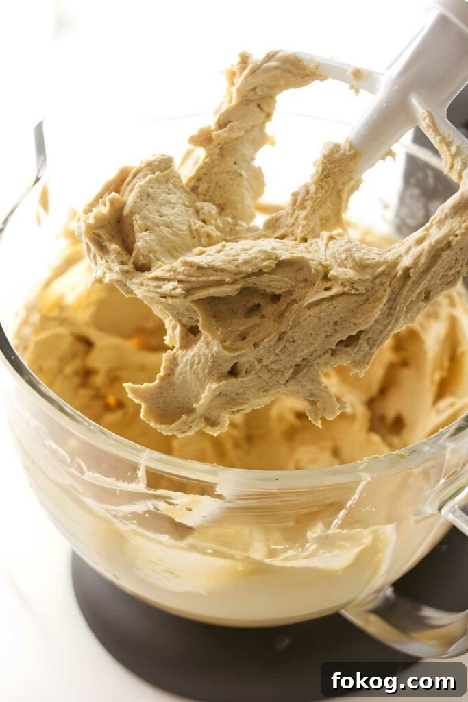 Close-up of creamy brown cookie dough in a bowl with spatula attachment.