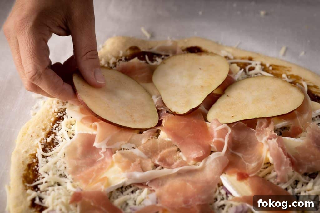 Pear slices being added to a deep dish pizza.