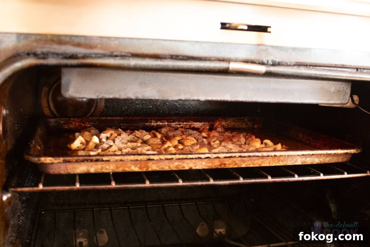 Steak and mushroom bites on an aluminum sheet pan under the broiler in an oven that could use to be cleaned.