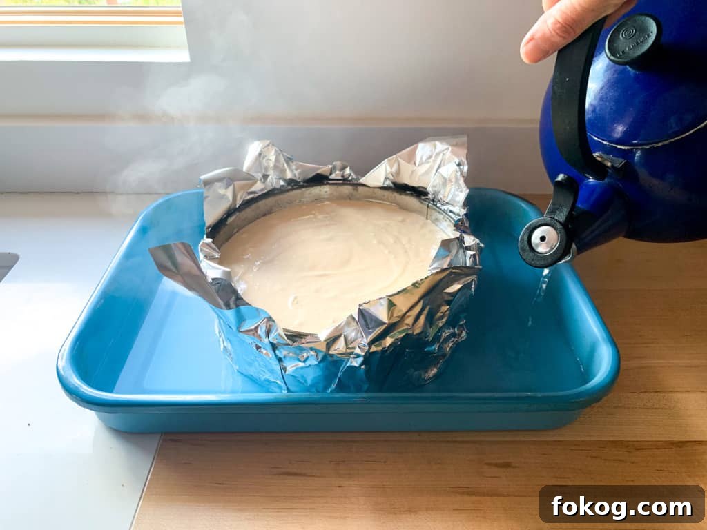 Cheesecake in a blue pan with hot water being poured into it. 