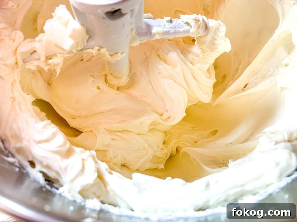A bowl of cream cheese being whipped with a paddle. 