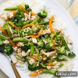Stir-fry with chicken, broccoli, and sugar snap peas served over white rice on plate.