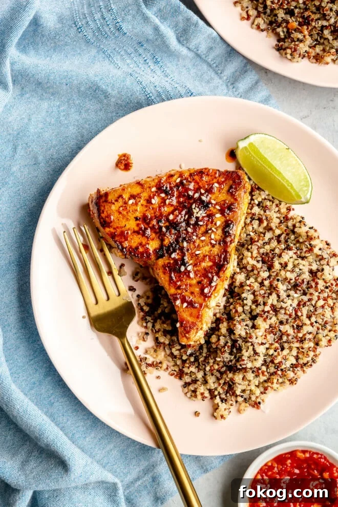 Chili-Lime Seared Ahi Tuna with Cilantro-Lime Sauce 2 Chili-lime seared ahi tuna steak on a plate next to a bed of tricolor quinoa and a lime wedge.