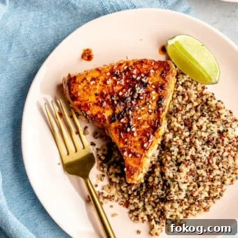 Chili-Lime Seared Ahi Tuna with Cilantro-Lime Sauce 15 Chili lime seared tuna steak on a light pink plate with a gold fork and side of quinoa with a lime wedge.