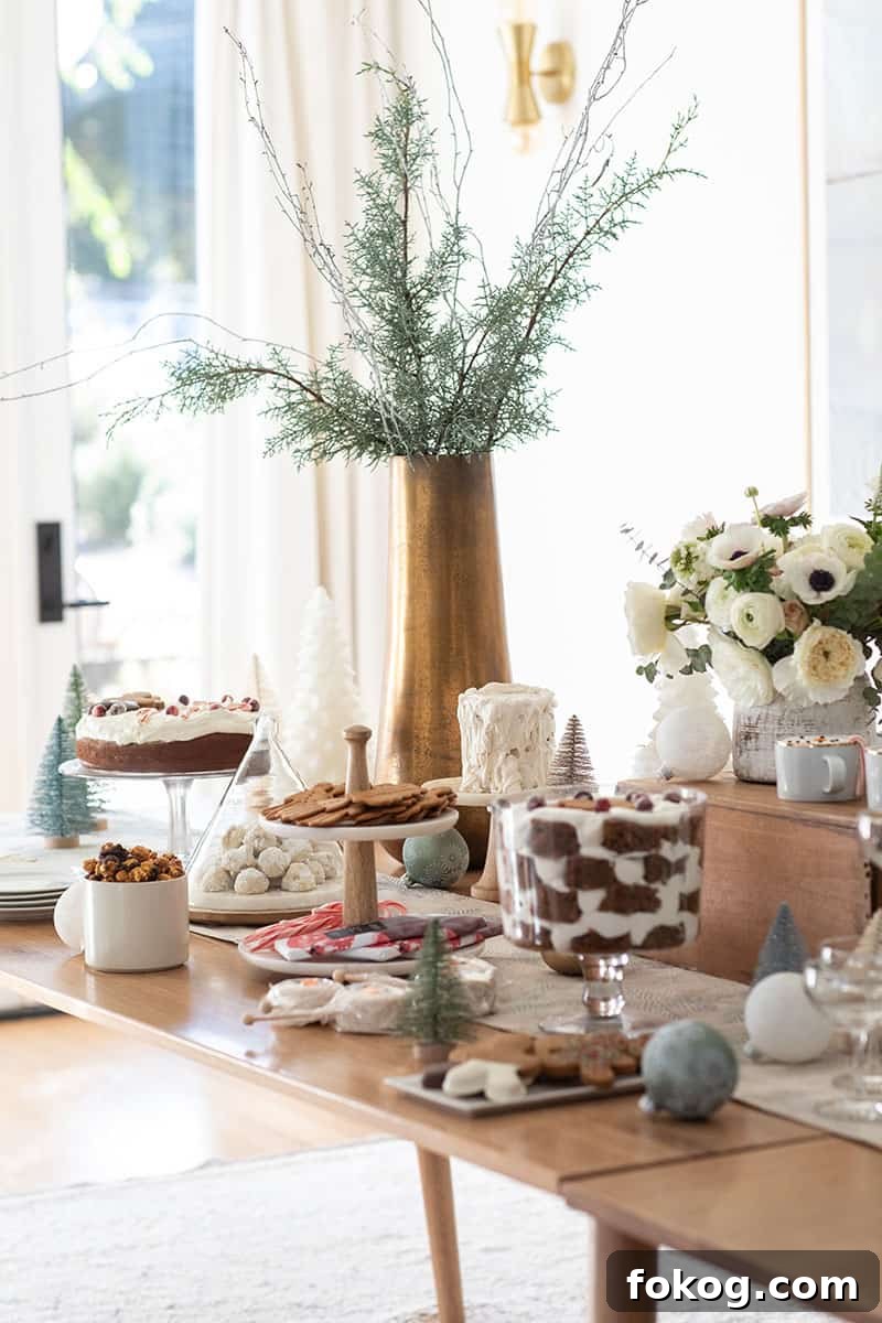 Christmas dessert table with cakes, cookies, flowers and brass vase with branches.