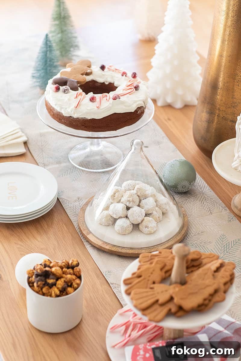 Christmas dessert table with a table runner, snowball cookies, gingerbread cake and cookies. 