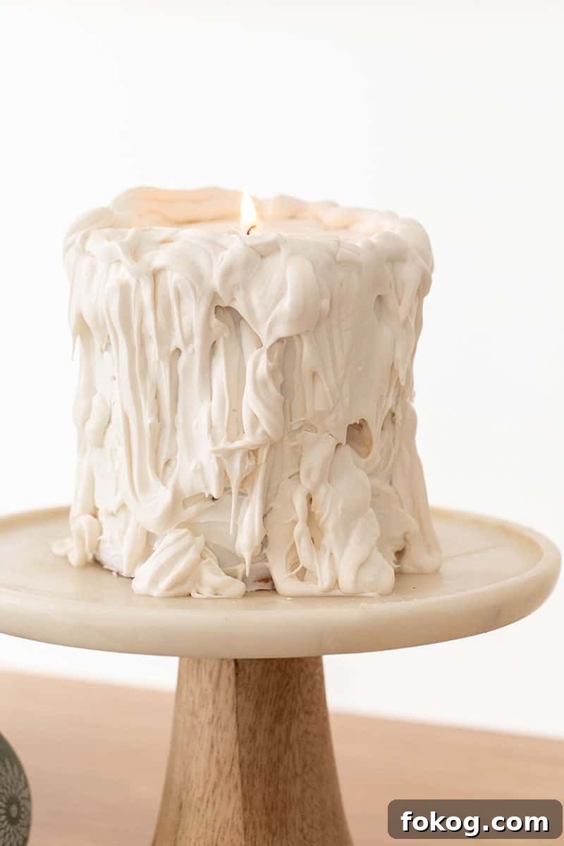 White candle drip cake on marble cake stand.