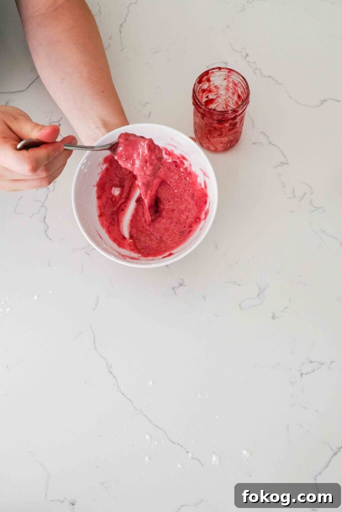 Bright pink cherry frosting drizzles off a spoon into a white bowl.