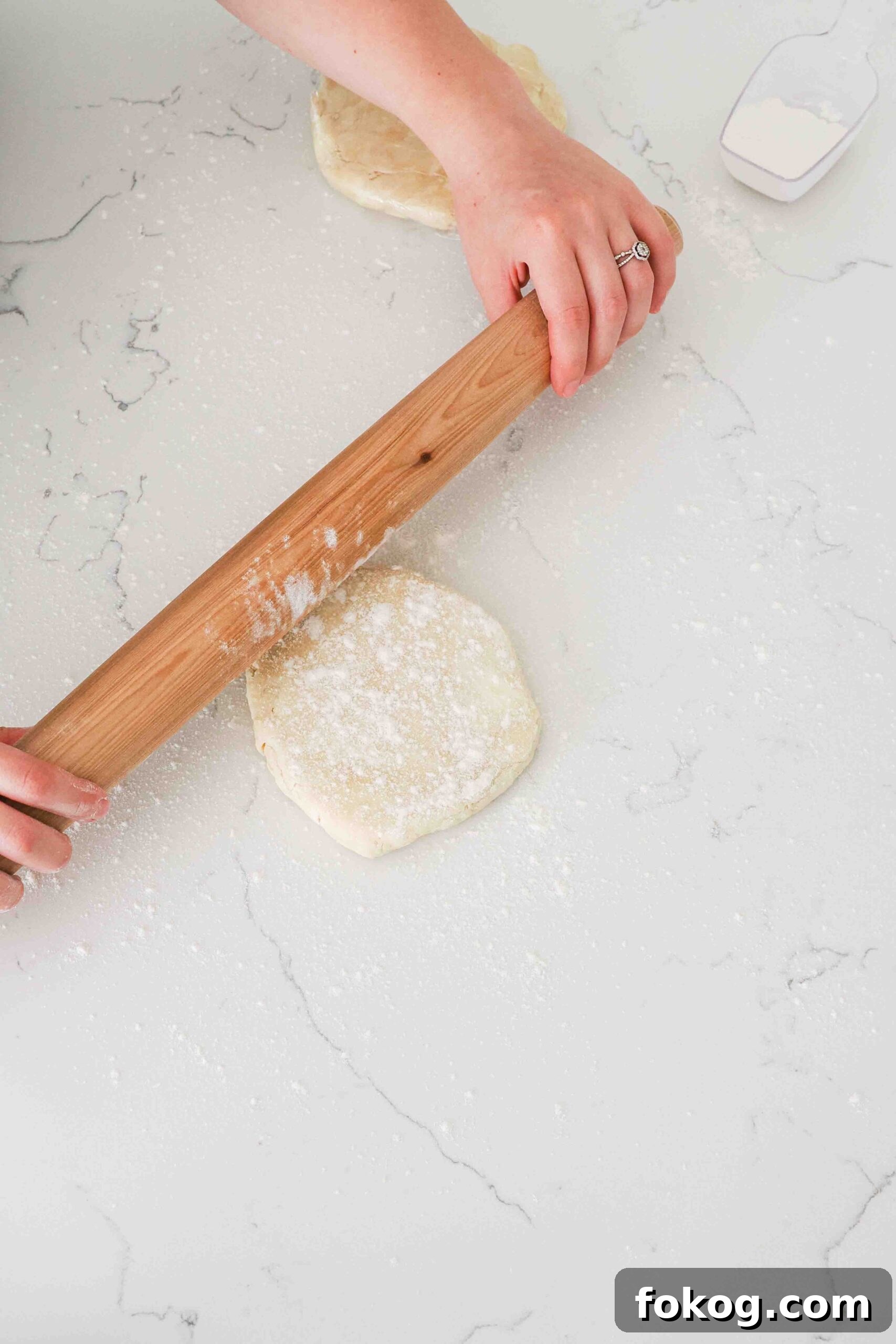 Two hands use a wooden rolling pin to flatten pie dough.