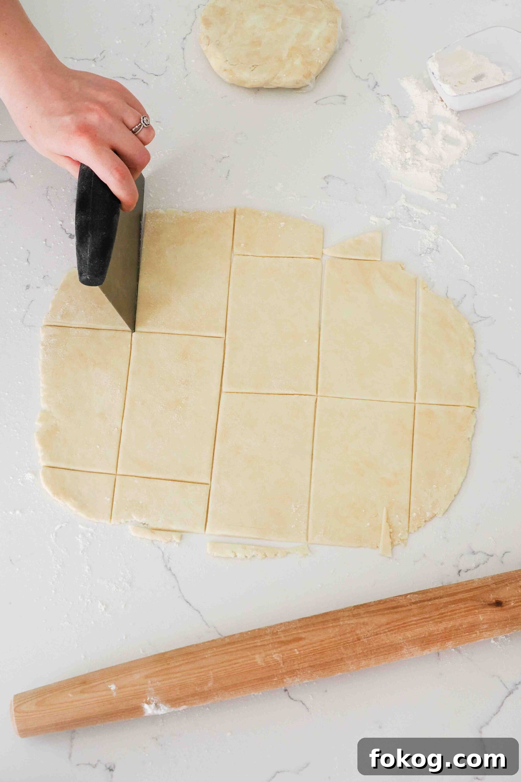 A hand uses a bench scraper to cut out rectangles of pie dough.