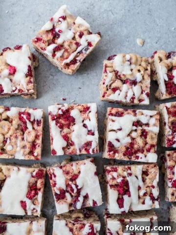 Cereal treats with raspberries and icing on a blue surface.