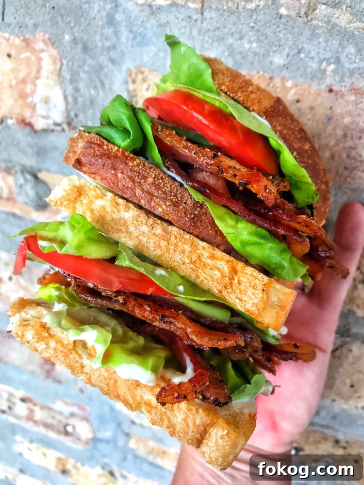 Another angle of two halves of a finished BLT being held in one hand, one above the other.