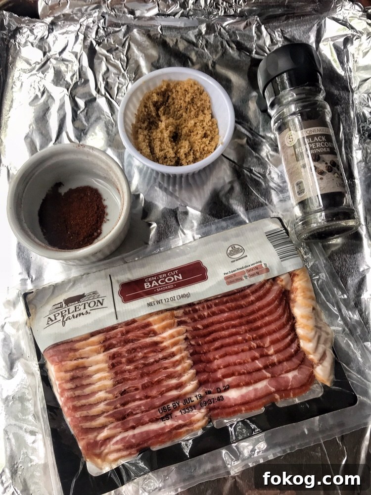 A baking sheet covered in foil. On top is a package of raw bacon, a black pepper grinder, a cup of brown sugar, and a cup of chili powder.