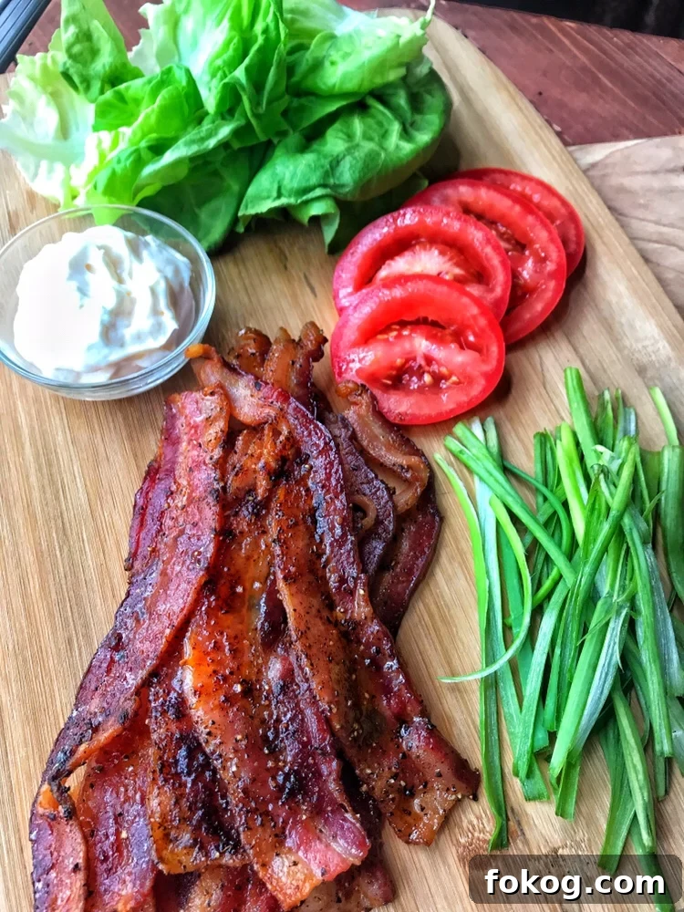 The cooked bacon on a cutting board next to mayo, sliced tomatoes, lettuce, and sliced scallions.
