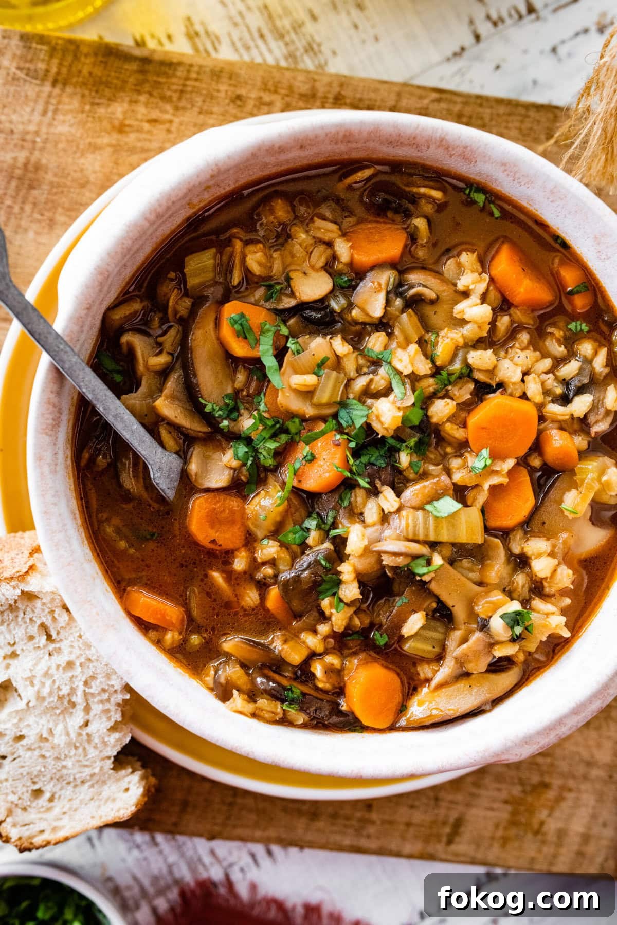 Mushroom Barley Soup Recipe in a soup bowl with a spoon ready to eat and crusty bread on the side. Spoon inside ready to take a bite.