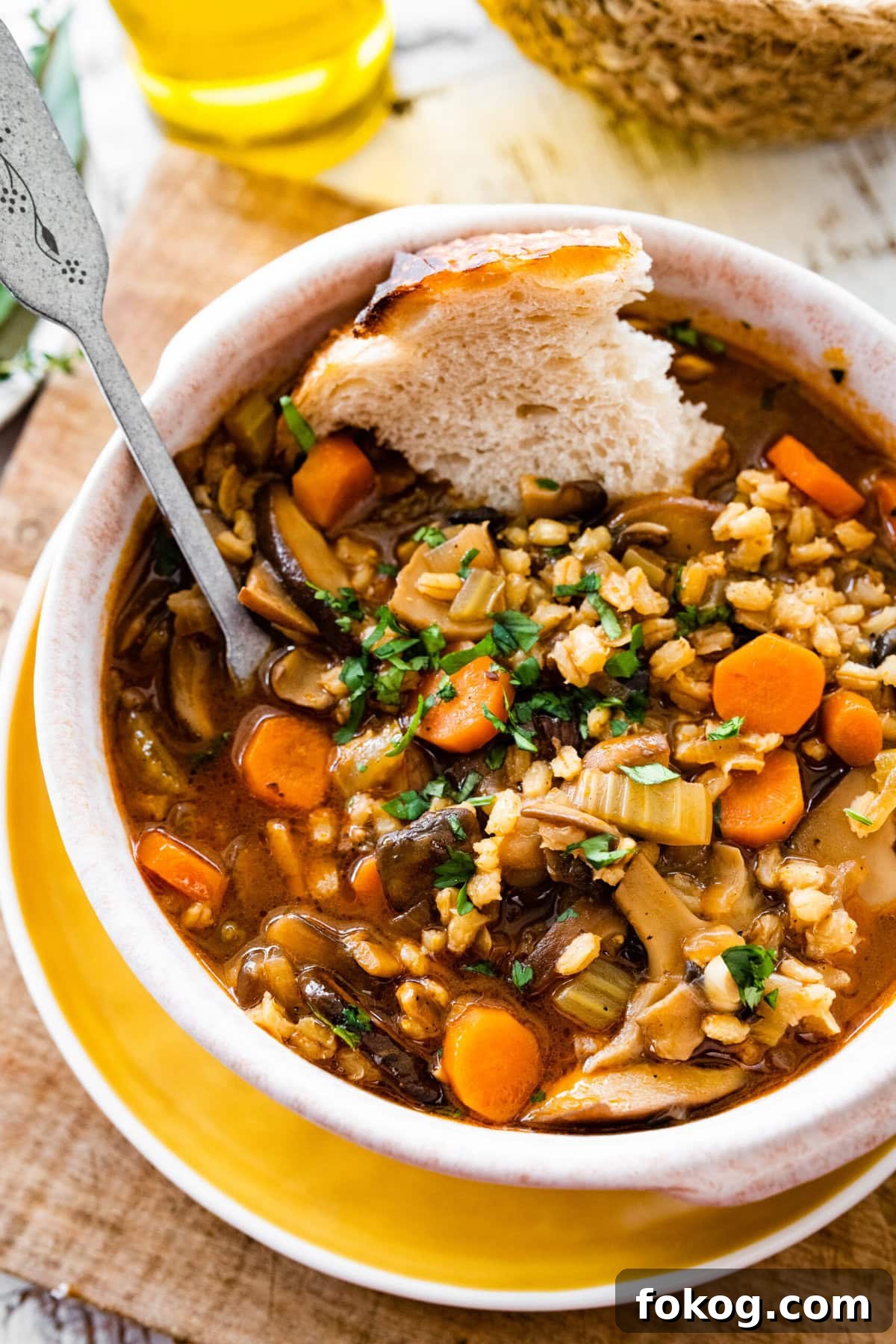 Spoon and bread in a bowl of mushroom barley soup.