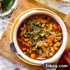 bowl of mushroom barley soup on a wooden board with a spoon ready to eat.