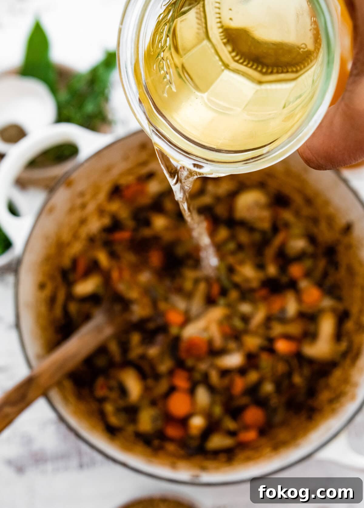 White wine pouring into a Dutch oven of cooked vegetables.