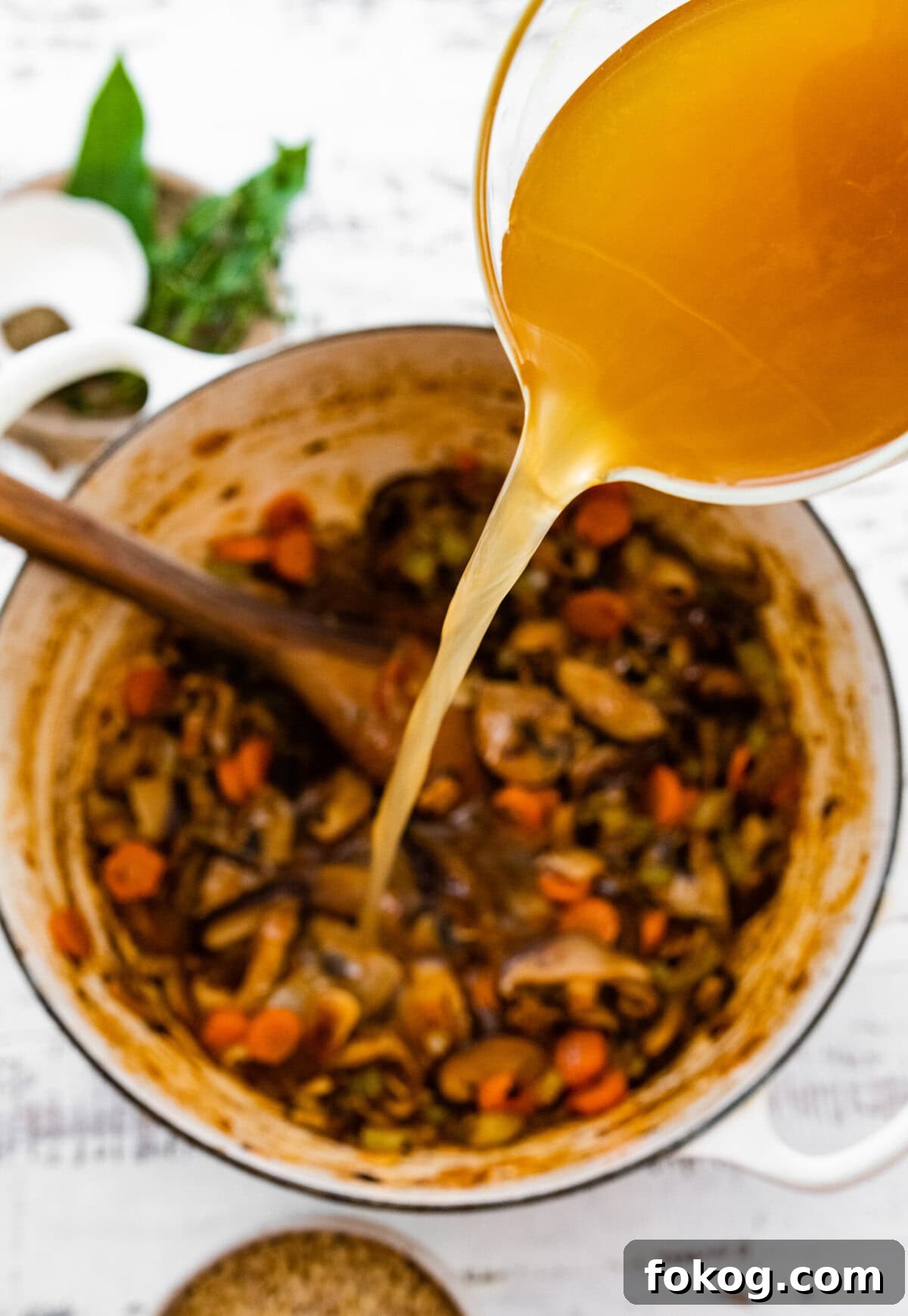 Stock pouring into a Dutch oven of cooked vegetables.