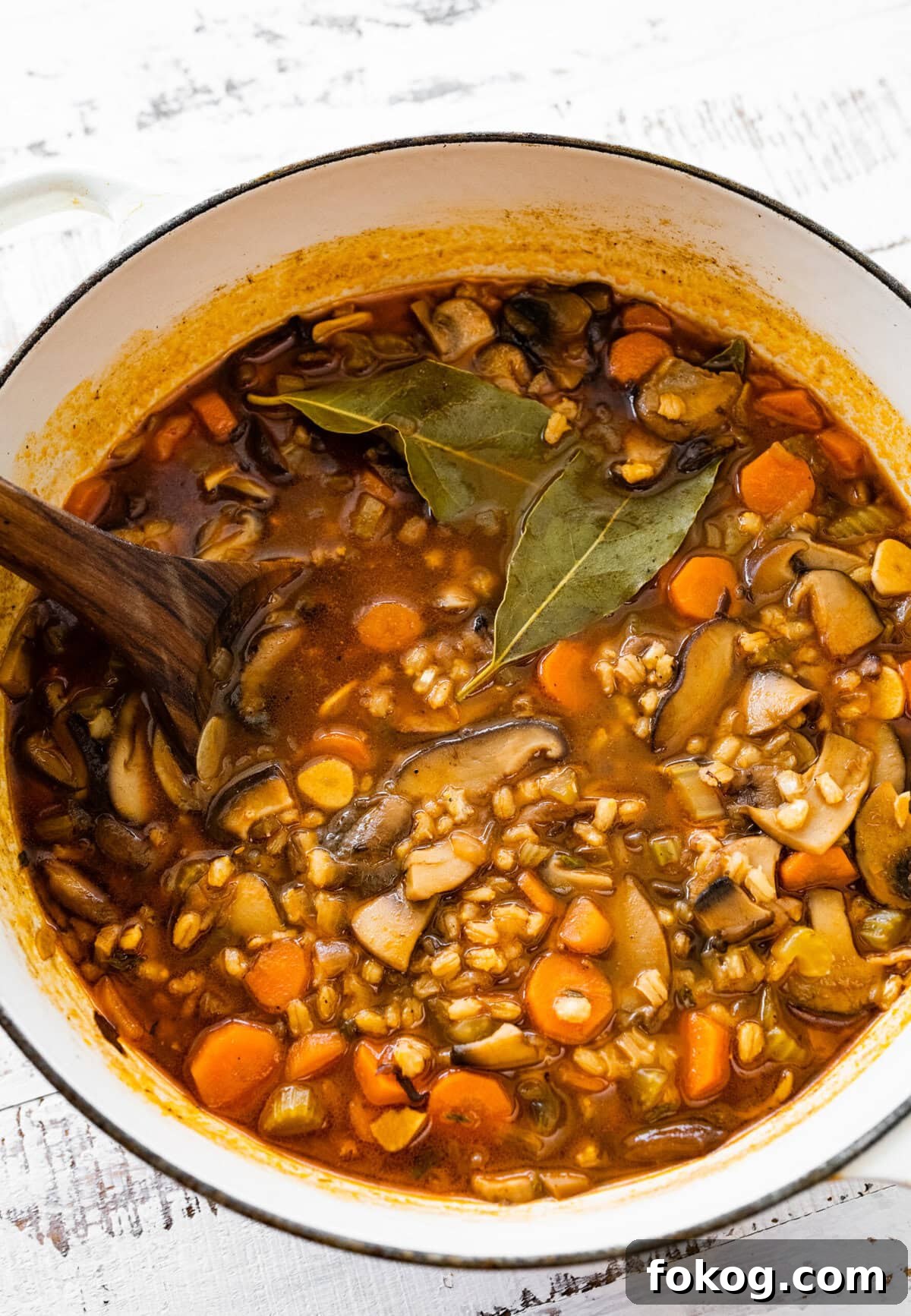 Wooden spoon in a Dutch oven of mushroom barley soup.