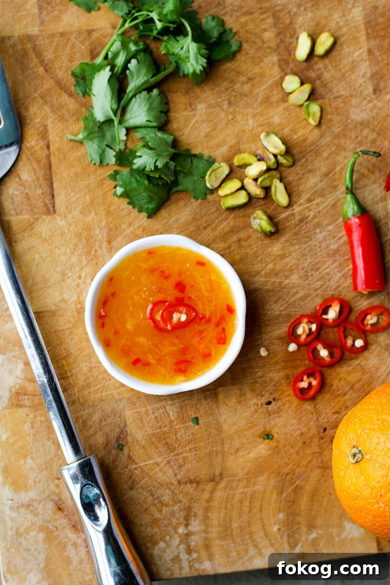 A cutting board with a ramekin of orange chili dipping sauce.