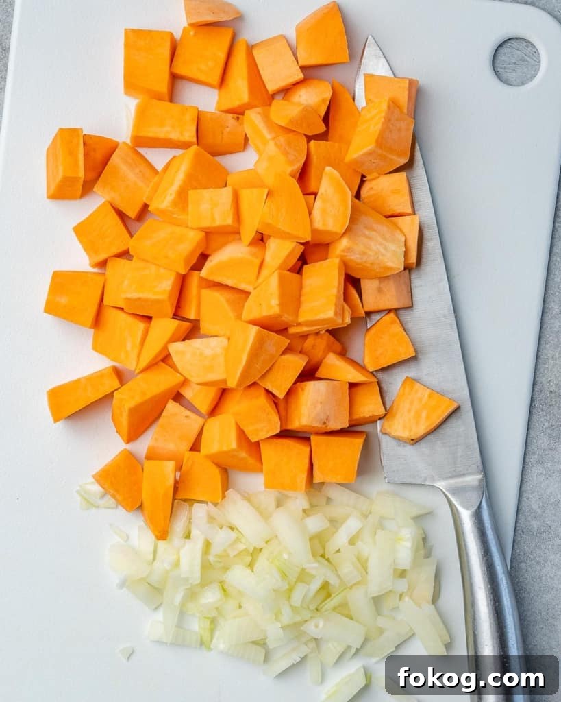 Chopped onions and sweet potatoes on a cutting board with a knife next to it