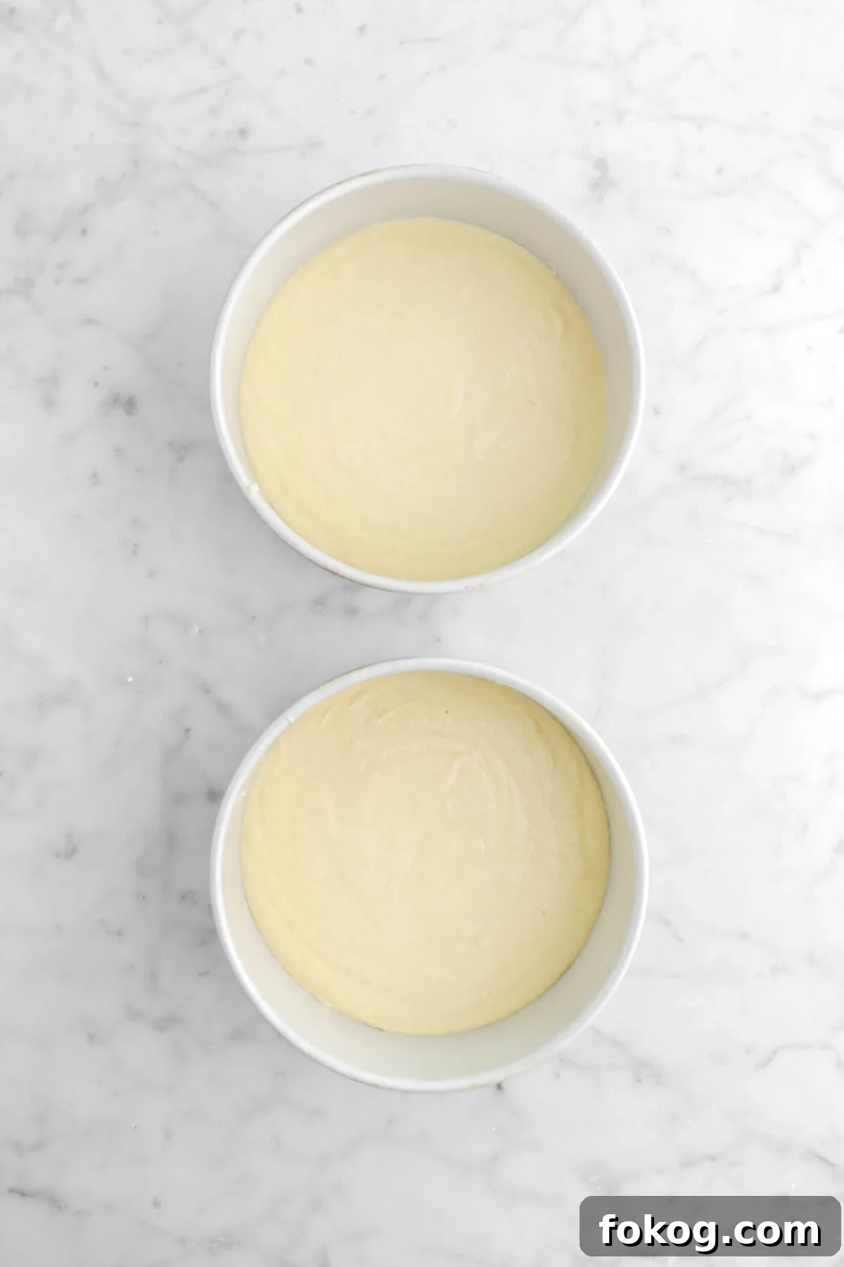 Classic Vanilla Cake with Smooth Buttercream Frosting 13 cake batter in two round cake pans on marble surface.