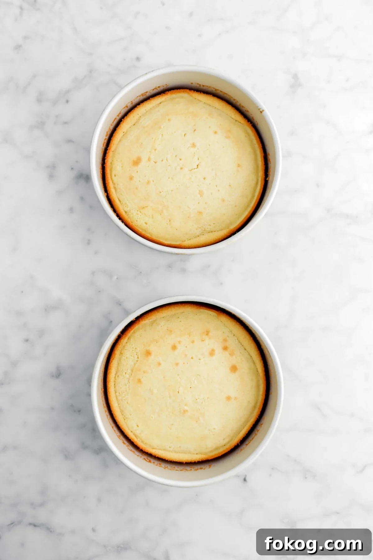 Classic Vanilla Cake with Smooth Buttercream Frosting 14 two baked vanilla cakes in round pans on marble surface.
