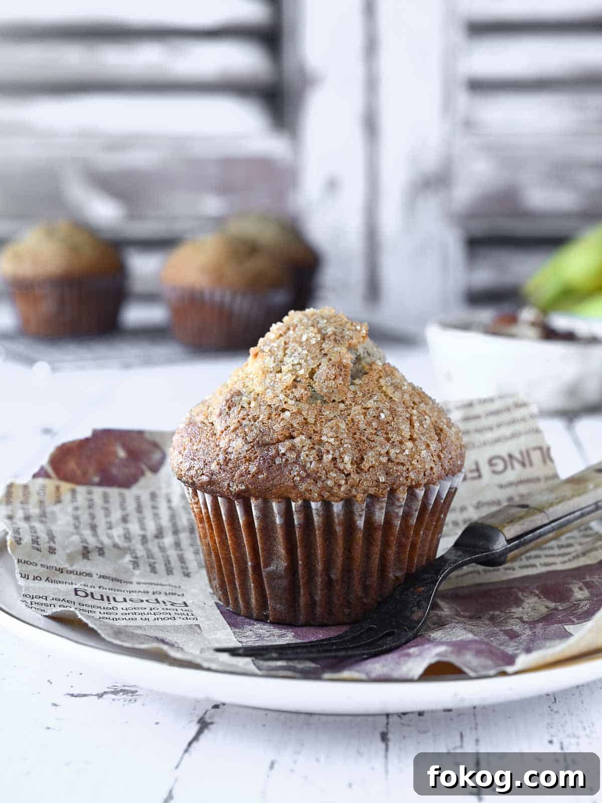 Moist Banana Pecan Muffins Recipe for Breakfast or Brunch 10 Banana muffin on a white plate with muffins and pecans in the background.