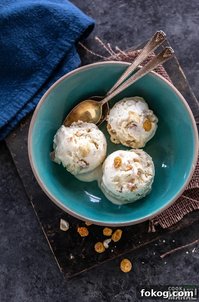 overhead shot of 3 ice cream scoops served in a blue bowl with few cashews and golden raisins scattered on the sides