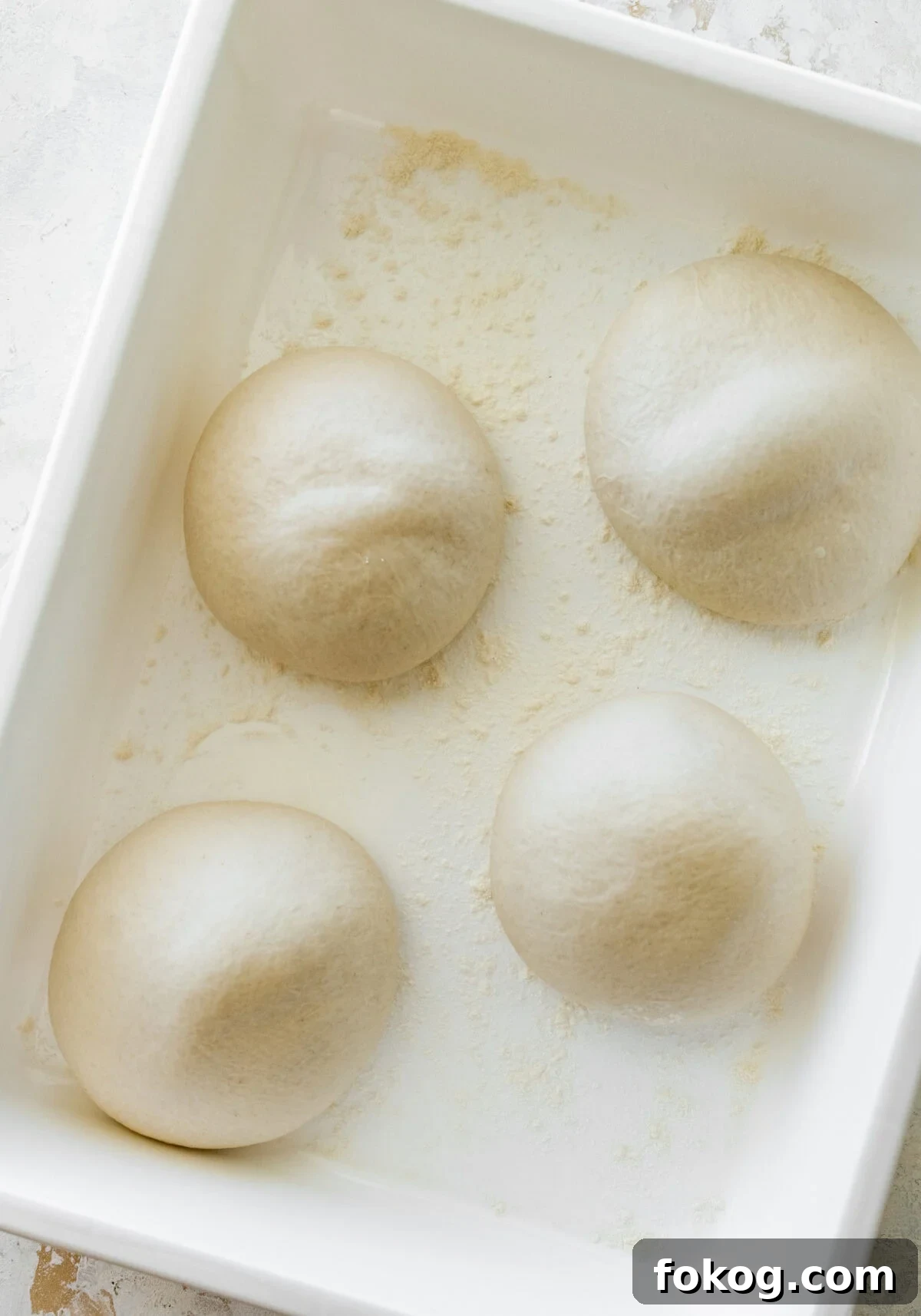 Four balls of dough in a white container that are risen.