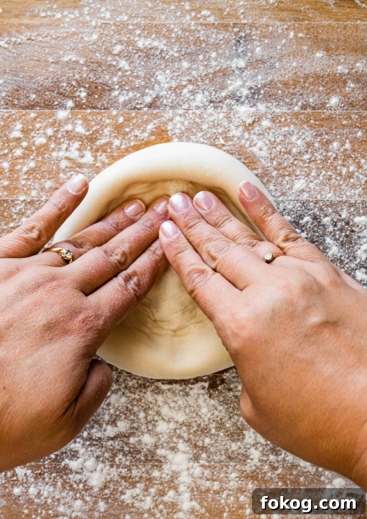 Hands of a woman kneading dough on a wooden table.